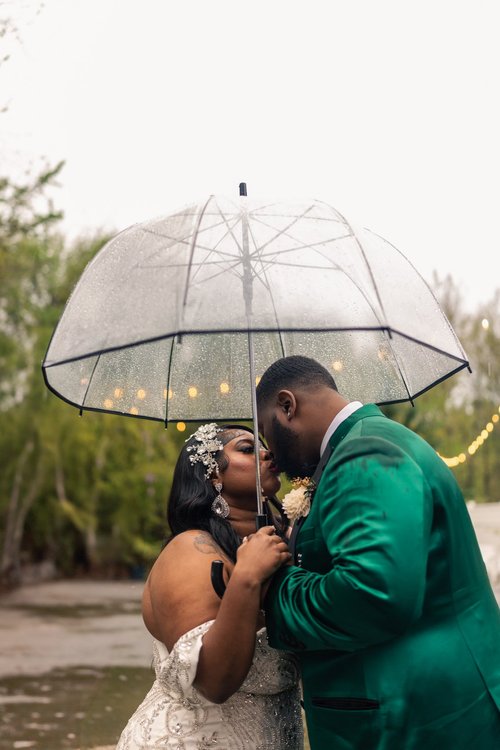 A couple shares a kiss under an umbrella on their wedding day.