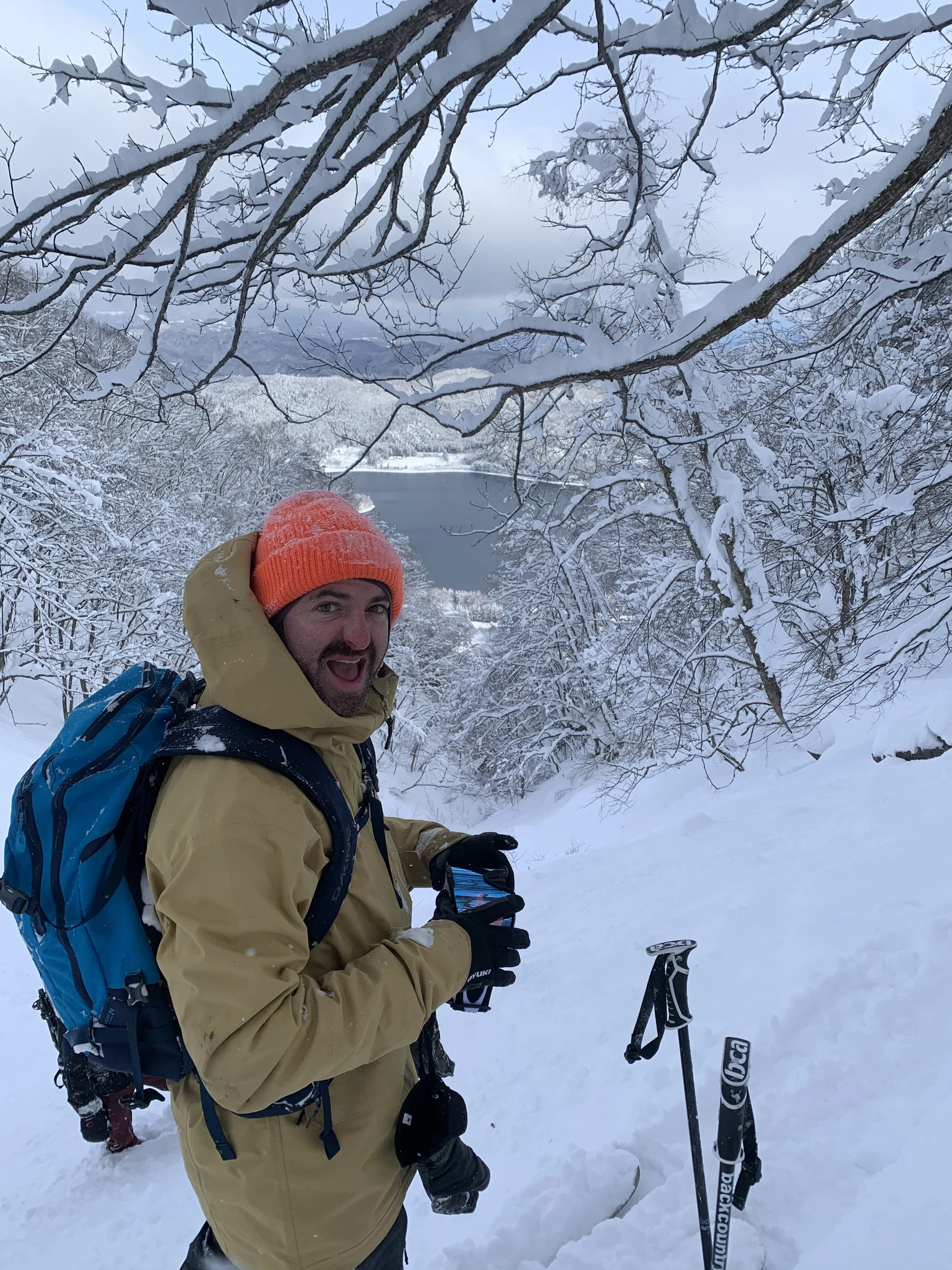 Man with snow jacket and orange beanie in the snow backcountry Hakuba lake Austin Toner