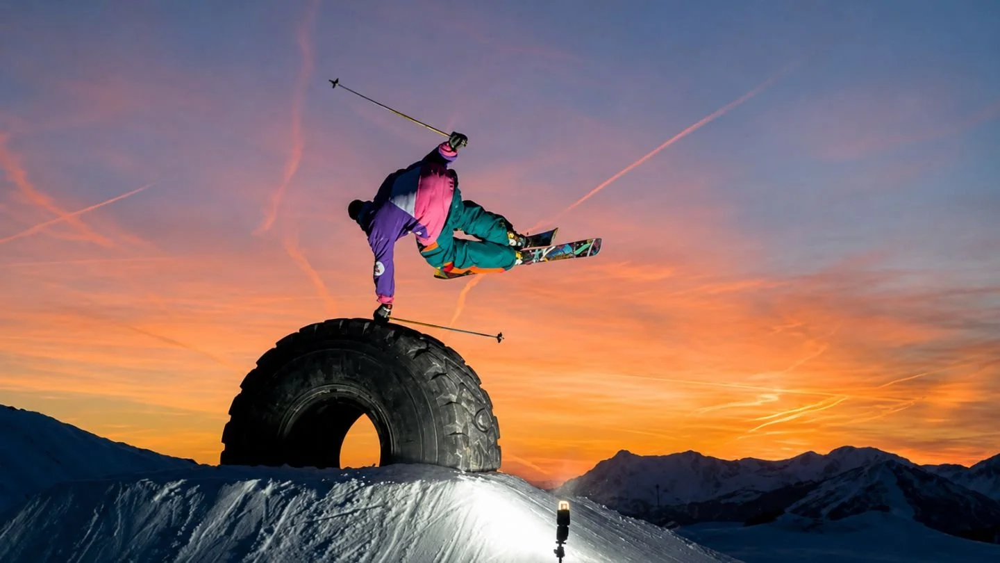 Skier performing a handplant over a large tyre at sunset
