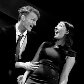 A man and woman laughing and interacting on stage during a performance.