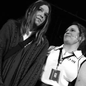 Two women, one with long hair and the other in a uniform, standing close together in black and white.