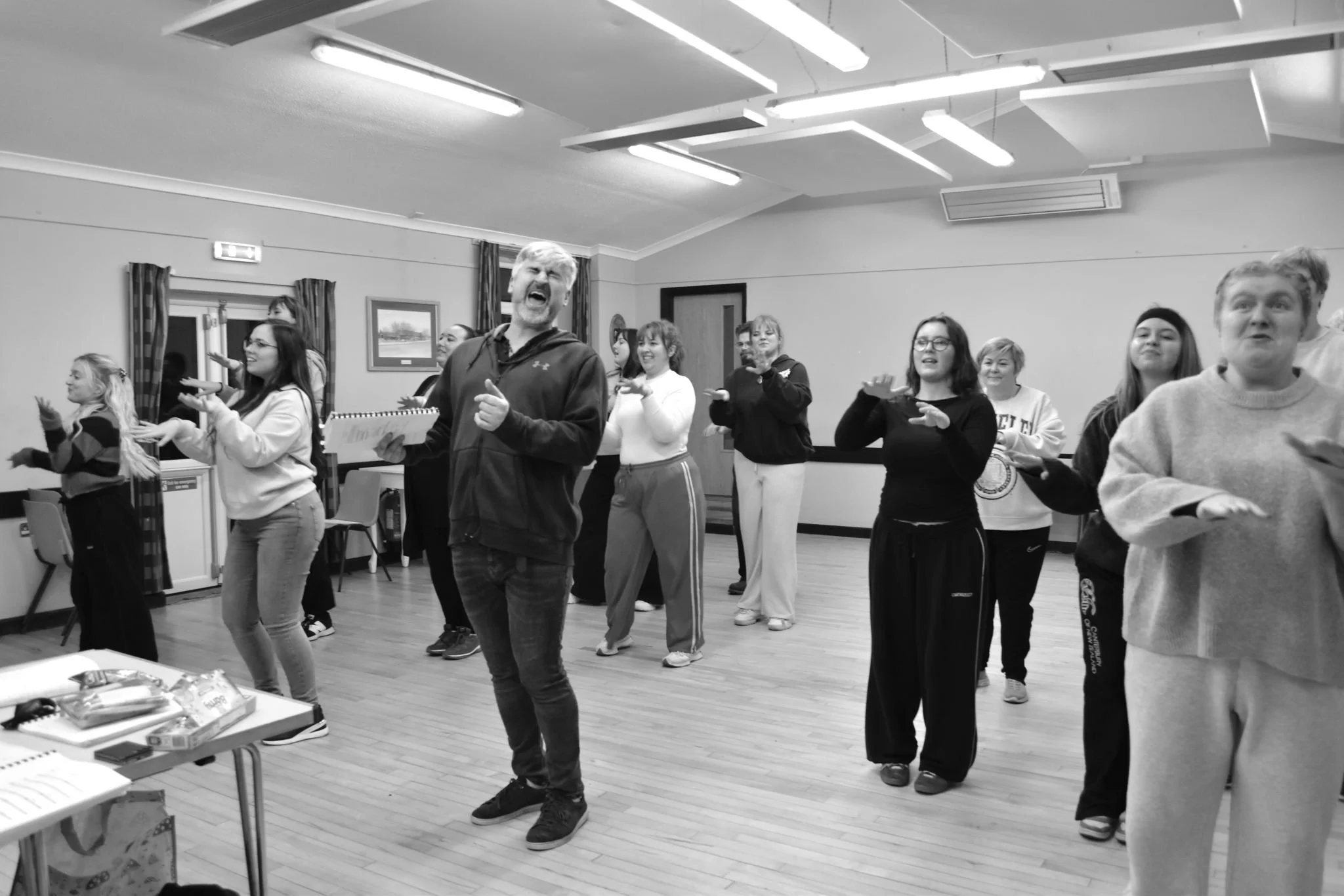 A group of people in a room appear to be singing or participating in a group activity, with expressive and joyful facial expressions.