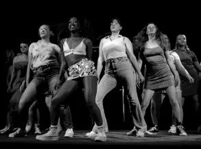 Group of diverse women dancing together on stage in casual attire.