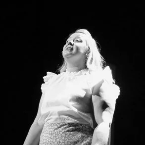 A woman smiling and looking upward, dressed in a light-colored outfit, in a black-and-white photo.