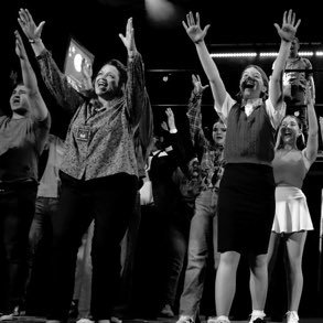 Group of diverse people cheering and raising their hands in celebration in a dark indoor setting