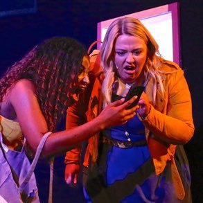 Two young women looking shocked at a phone together on stage