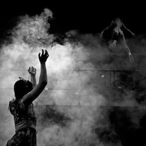 Person raising hands in a smoky environment with a mountain in the background.