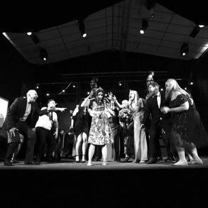 A group of people on a stage, some holding hands, participating in a dance or performance under stage lights.