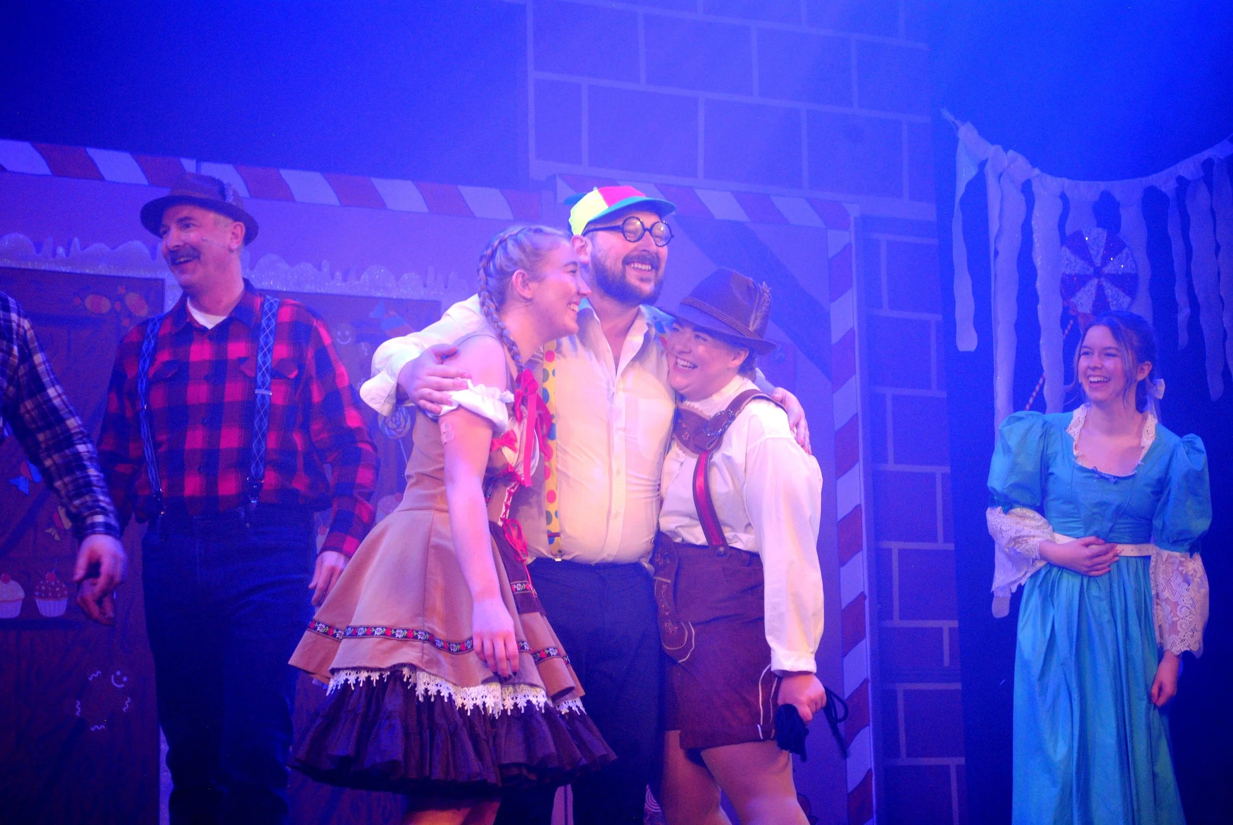 People dressed in costumes on stage, smiling and hugging, in a theatrical setting.