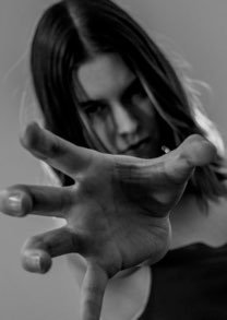 A woman with dark hair reaching out toward the camera, with a serious expression.