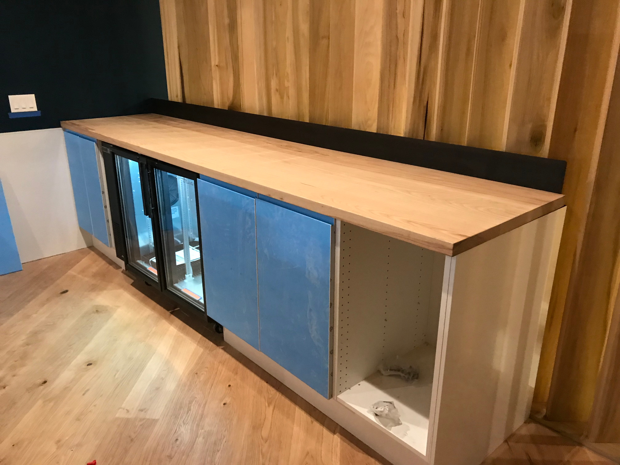 A wooden counter top being installed on top of a mini fridge area.