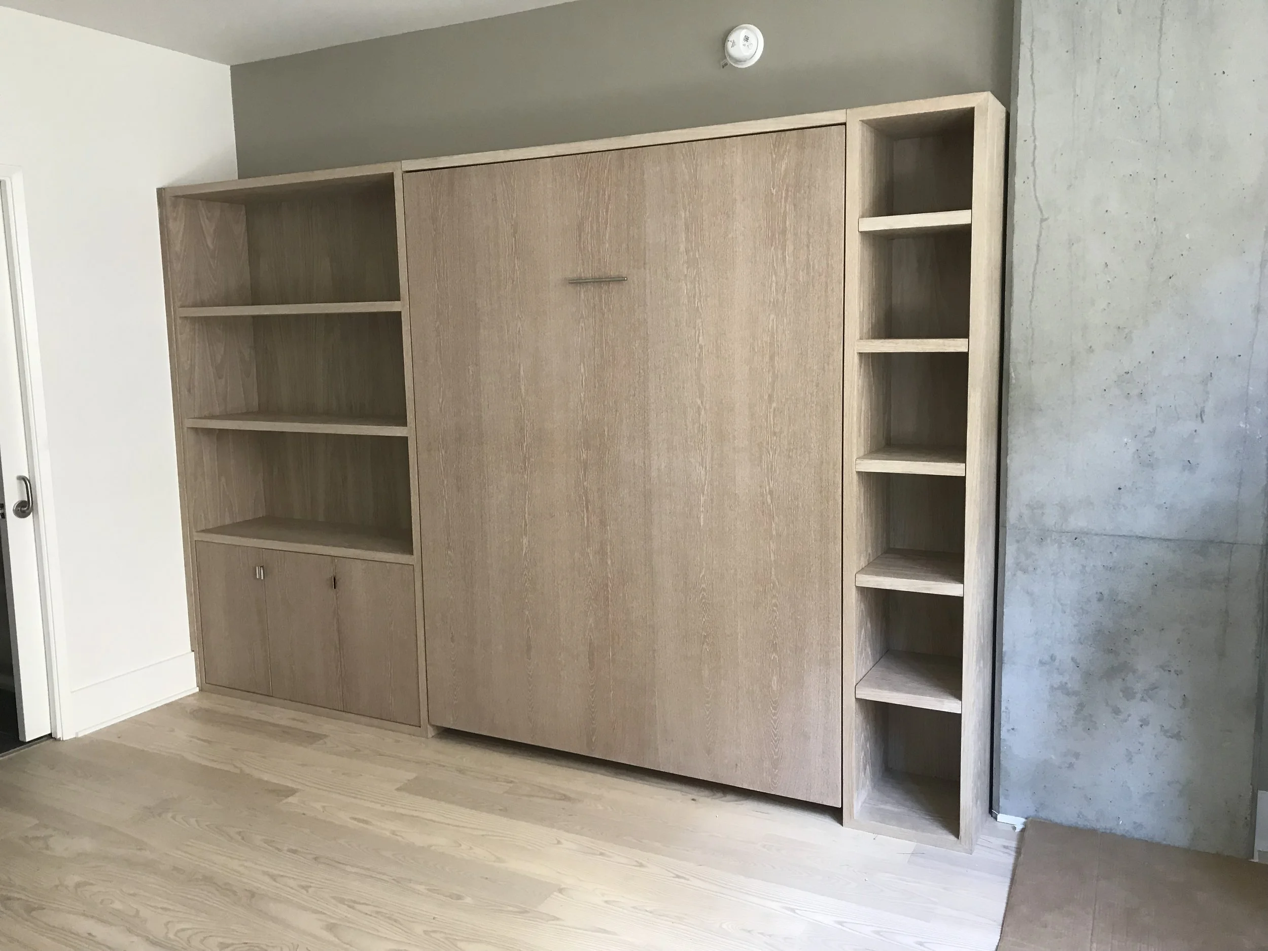 A wooden fold away bed with shelving space on each side of the bed. The bed is folded away.