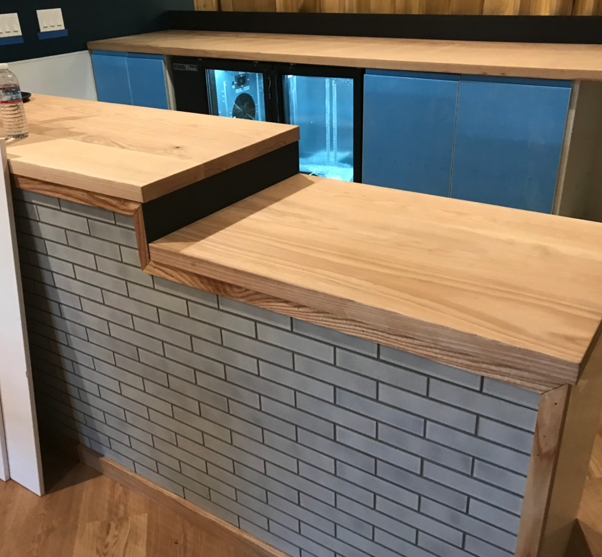 A large, multi layered counter top with a wooden top and a grey brick like design in front.