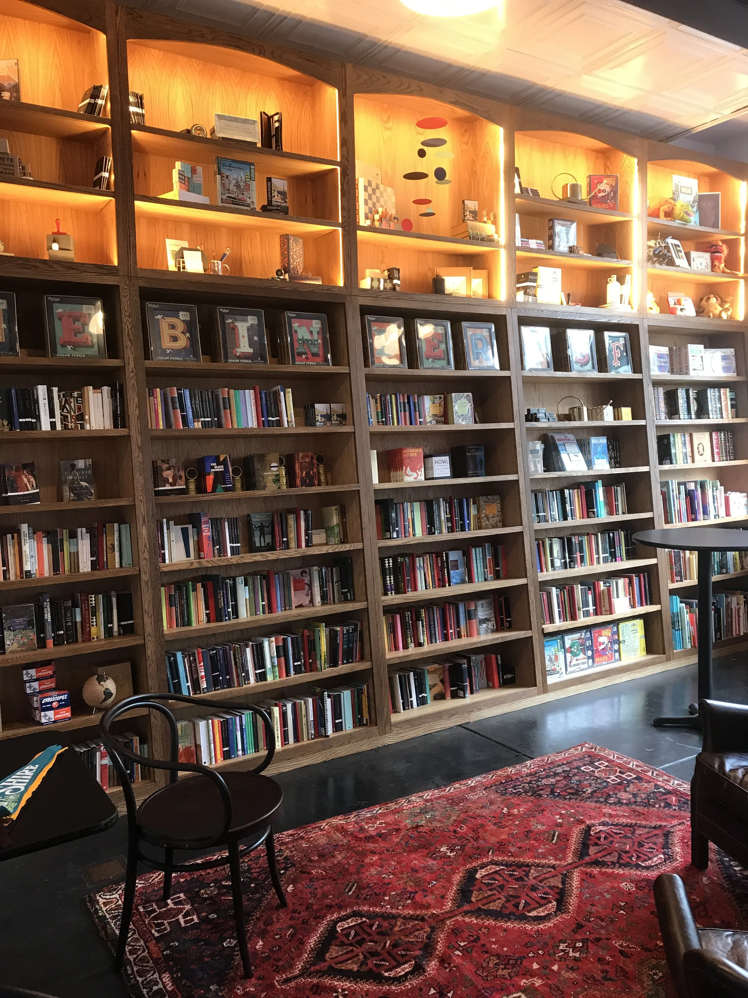 Many rows of shelving for books with smaller shelves above for displays and holding books. The smaller top row is lite up with stripe lights.