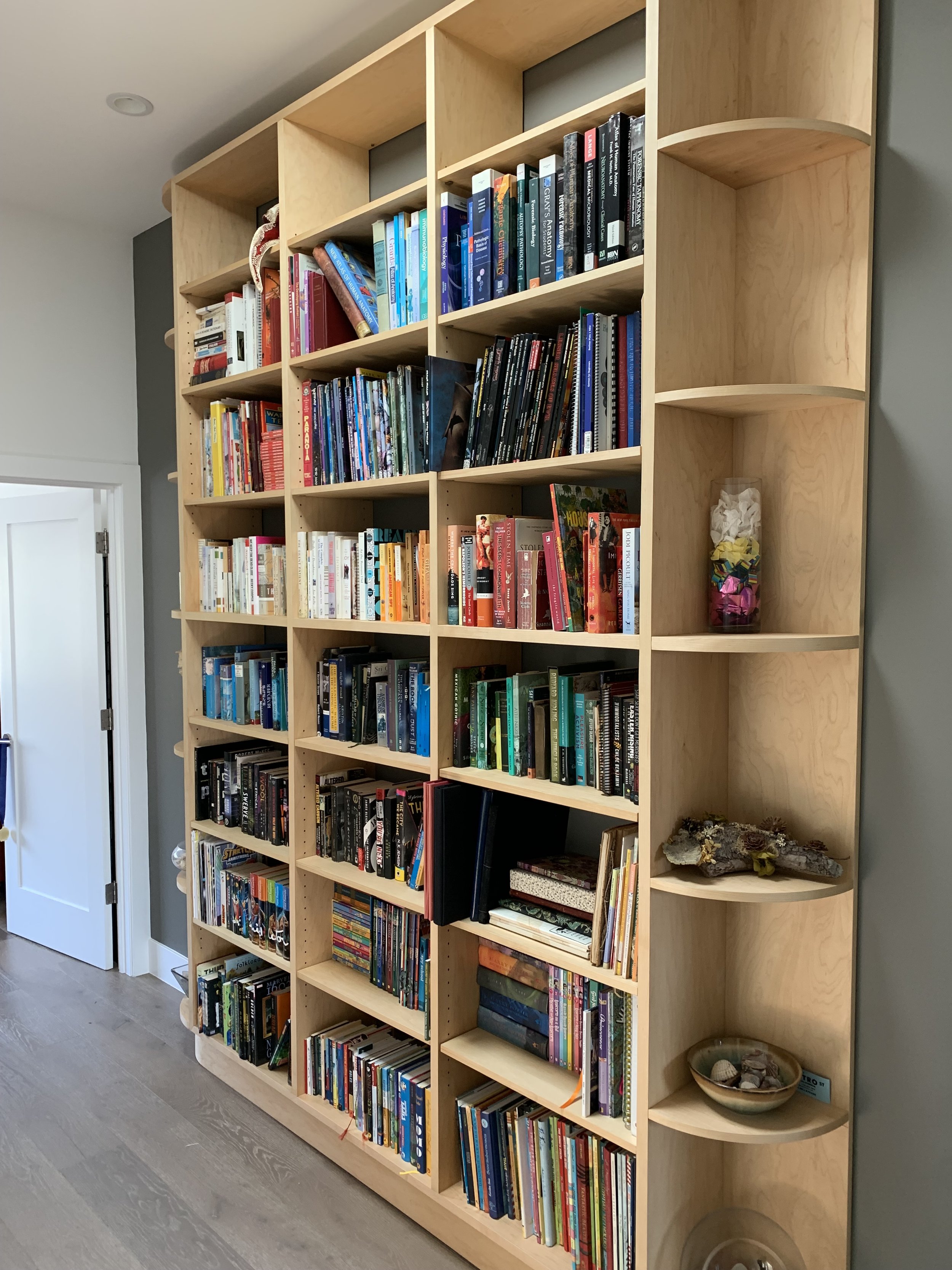 A large wooden bookshelf filled with many books. The ends of the shelves are curved into a quarter circle shape.