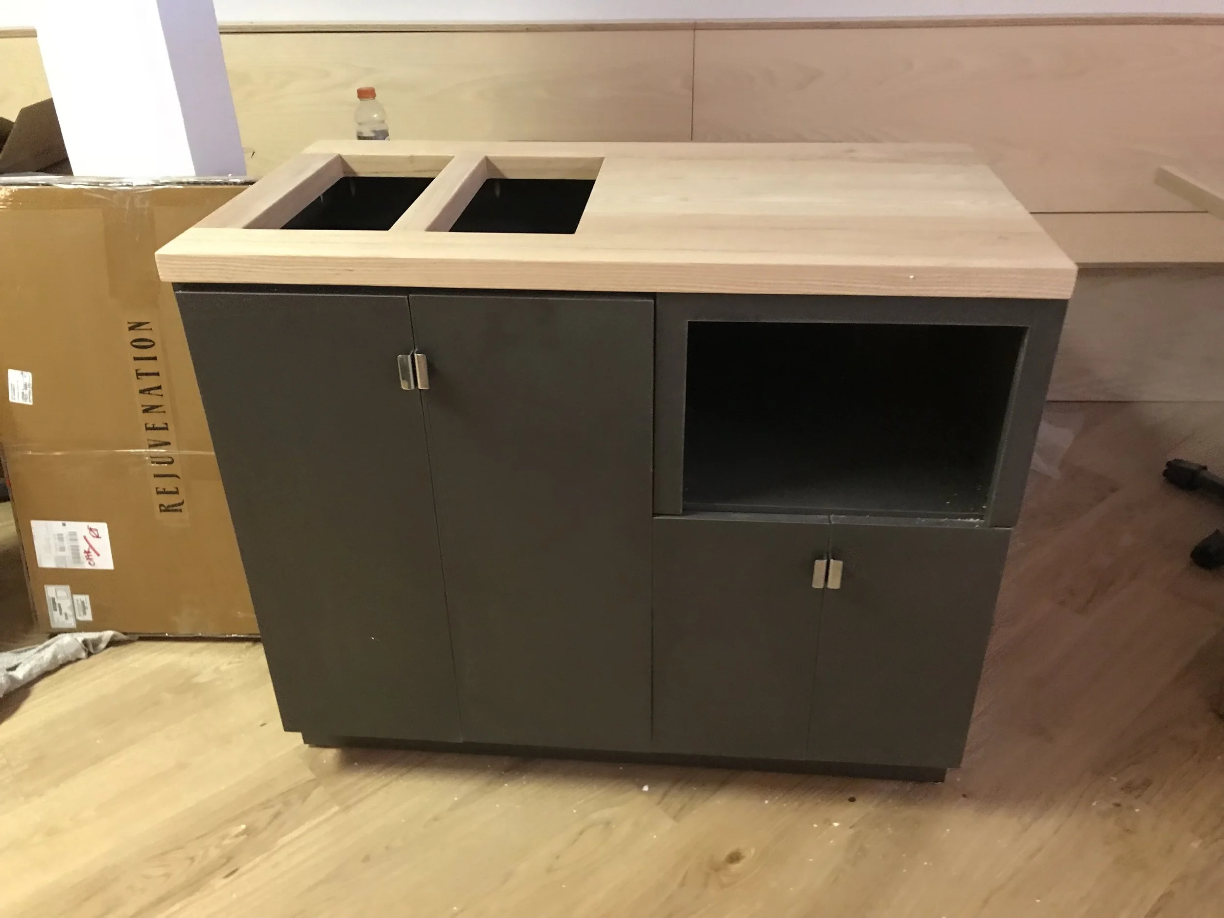 A custom portable bin, its body is a dark grey while the top is made of a light coloured wood.
