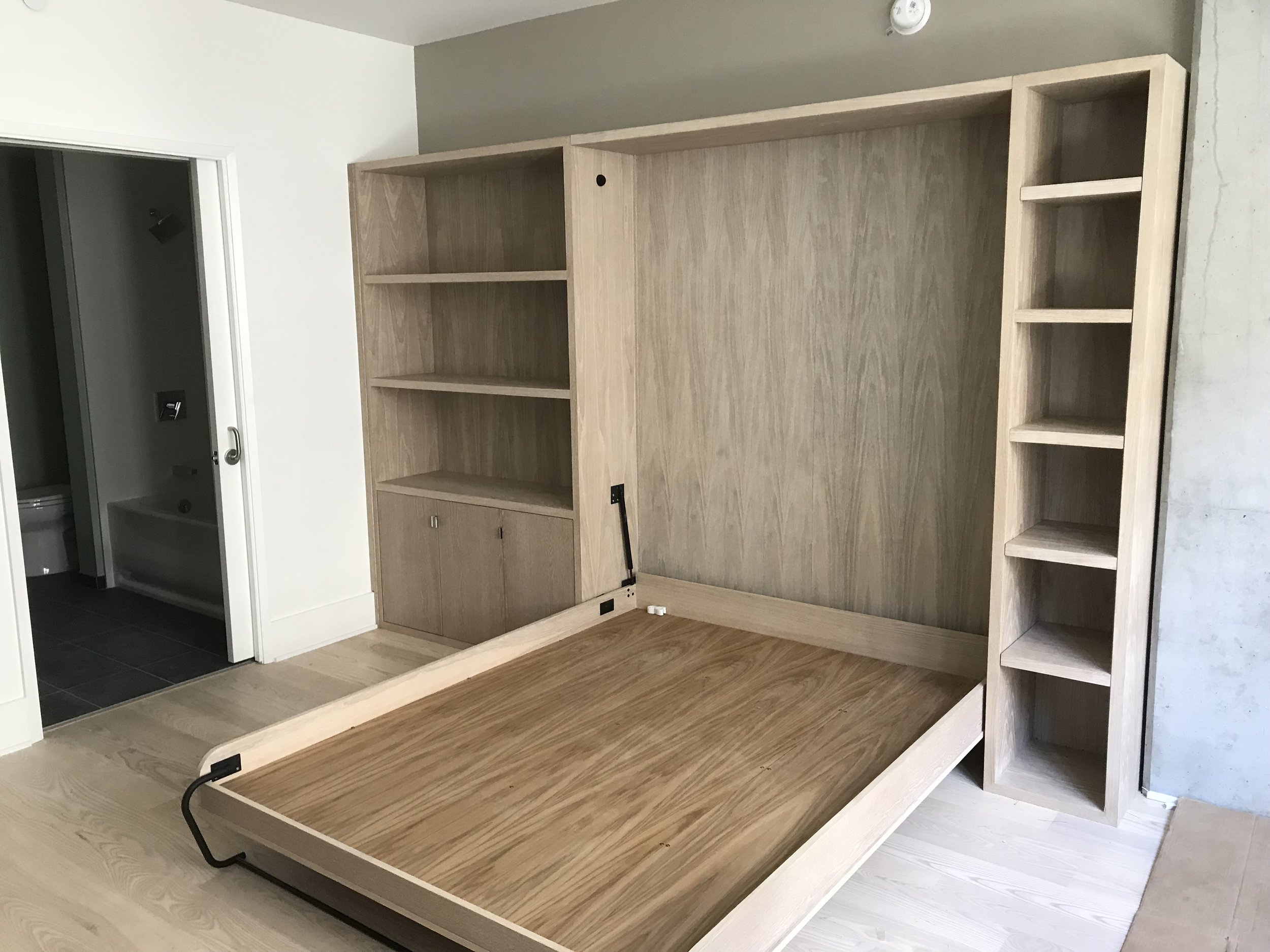 A wooden fold away bed with shelving space on each side of the bed. The bed is folded out.