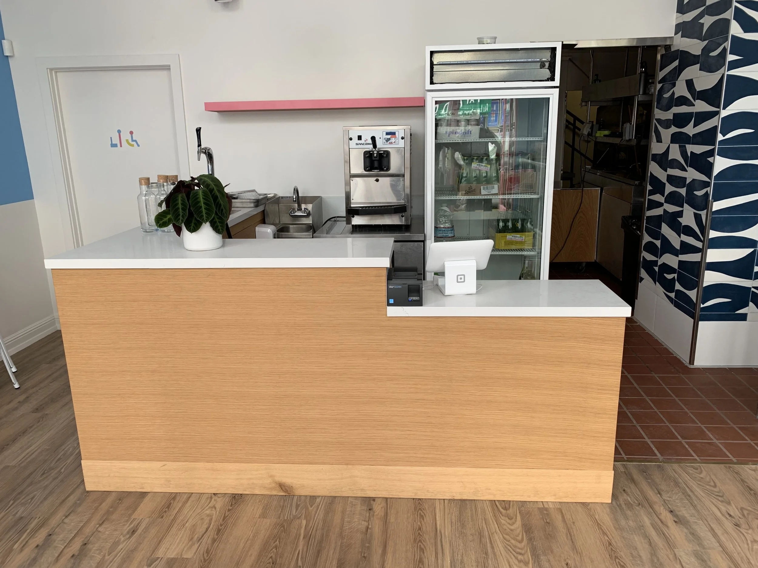 Front view of a large L shaped counter with a wooden base and a white plastic counter top.