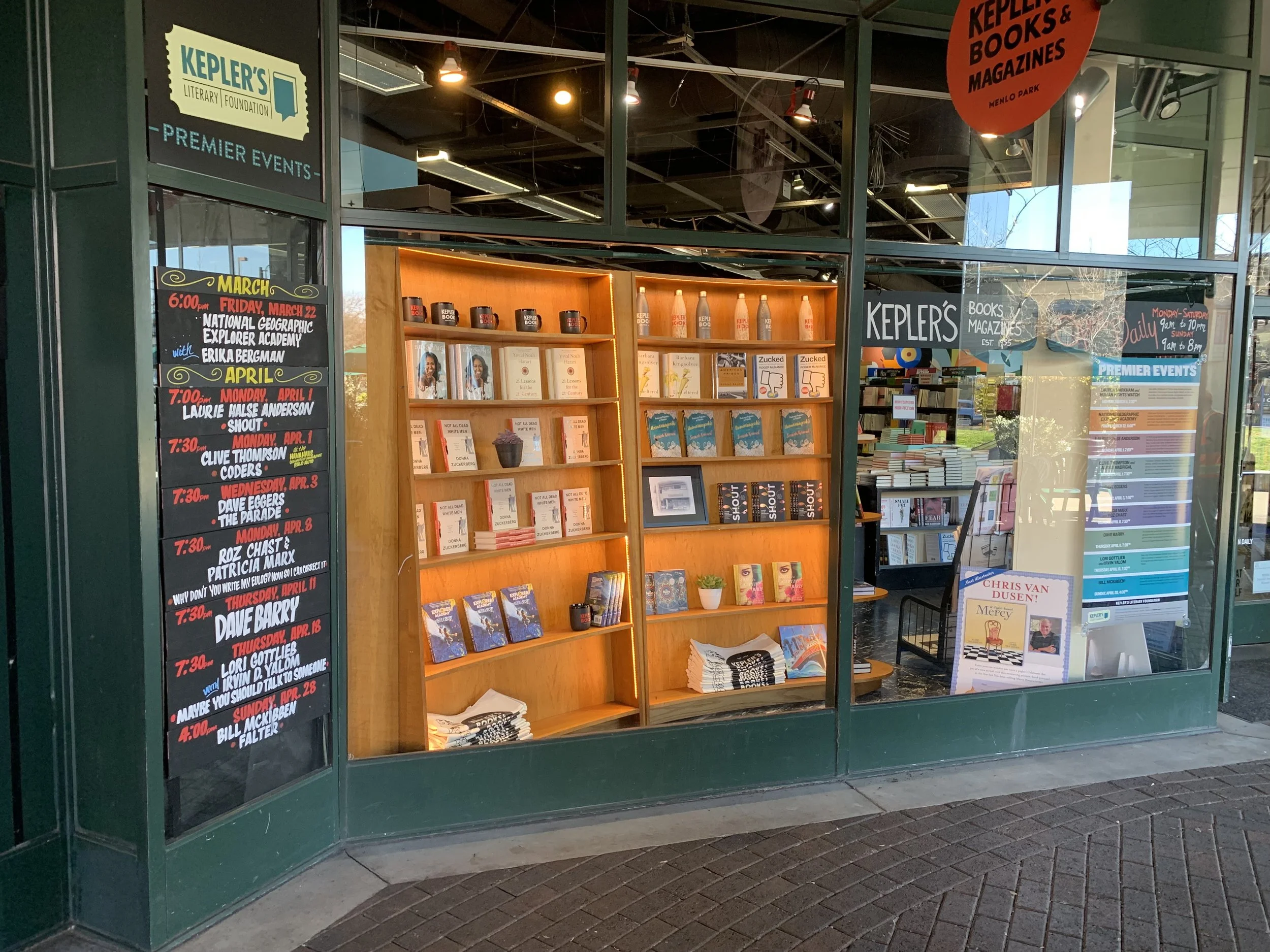 The front of a book shop with 2 large wooden book shelve displays in the middle windows.