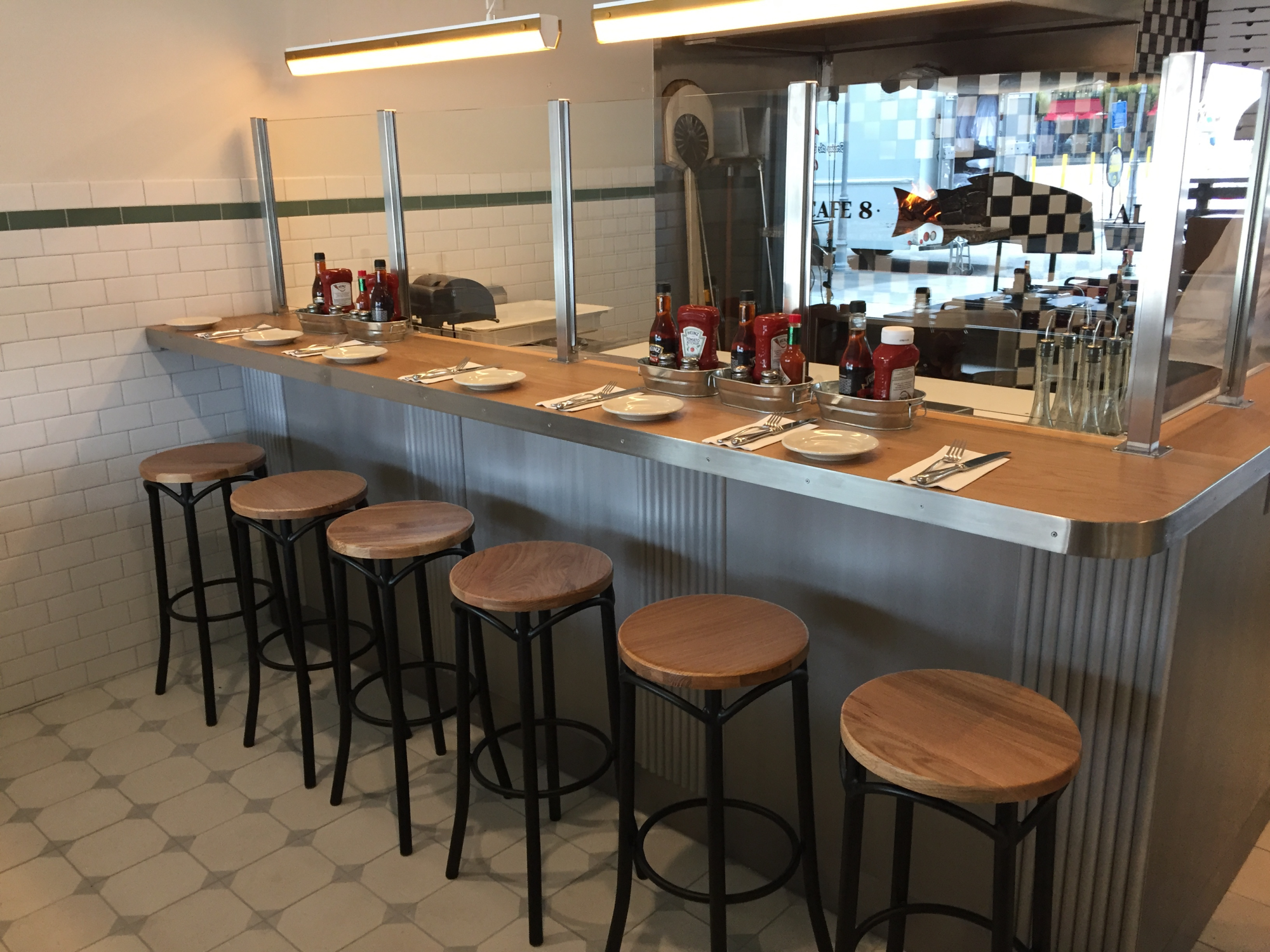A bar table for a restaurant, the bar has a side for preparing food while the other side has a stool area for patrons.