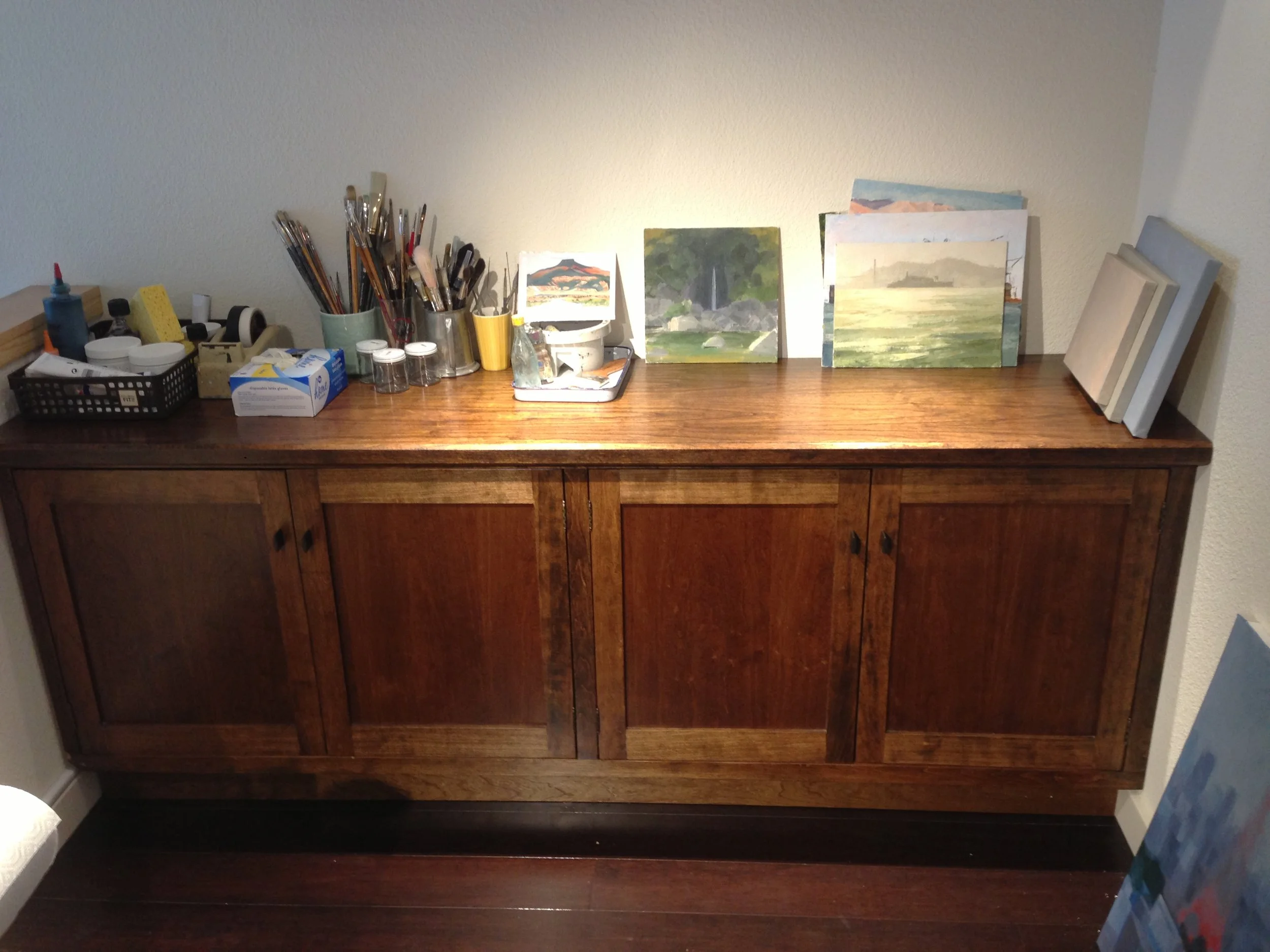 A long wooden cupboard with paint materials and canvases.
