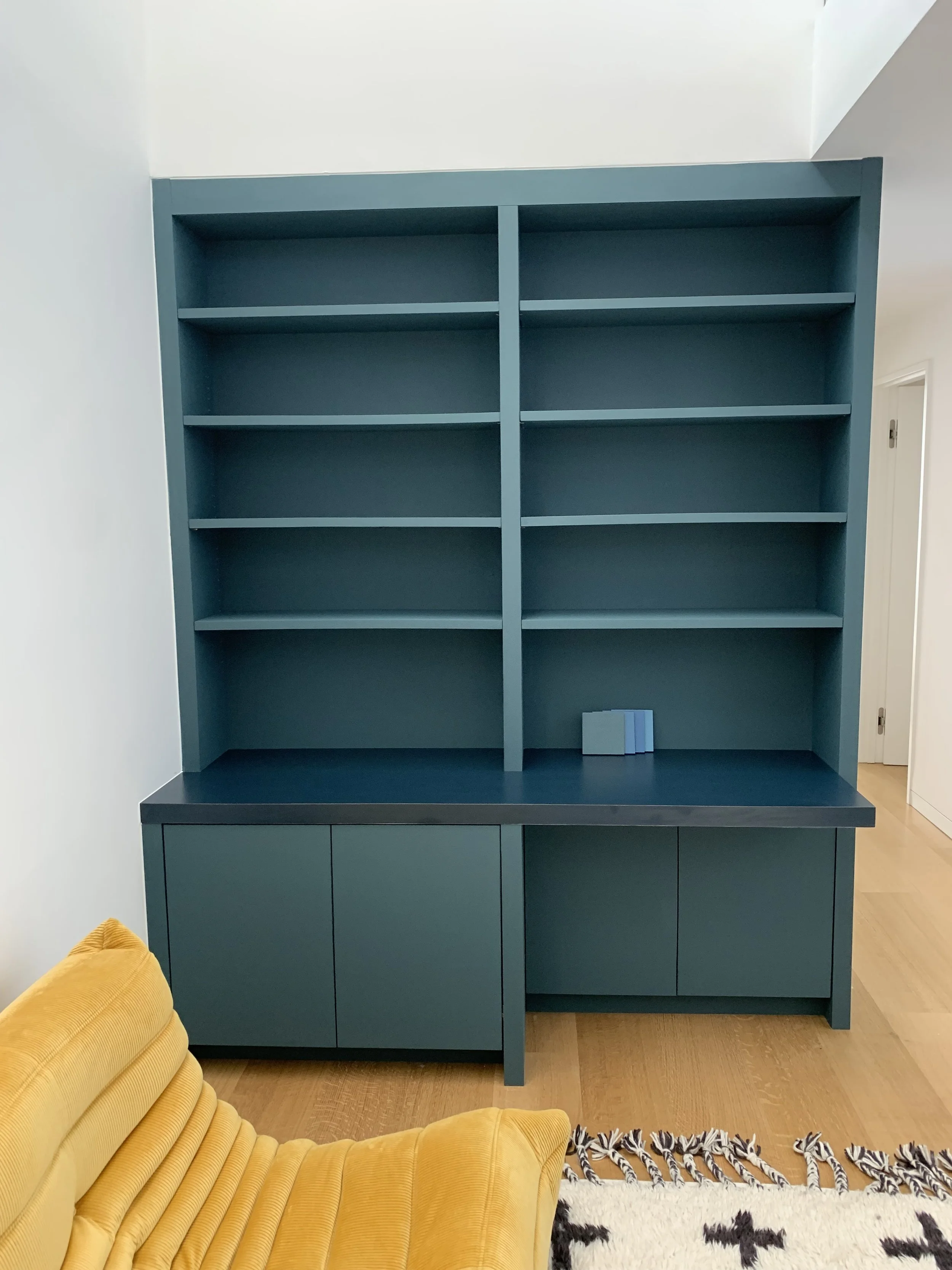 Large teal/blueish green cupboard and shelves are fitted in a corner of a residential seating area.