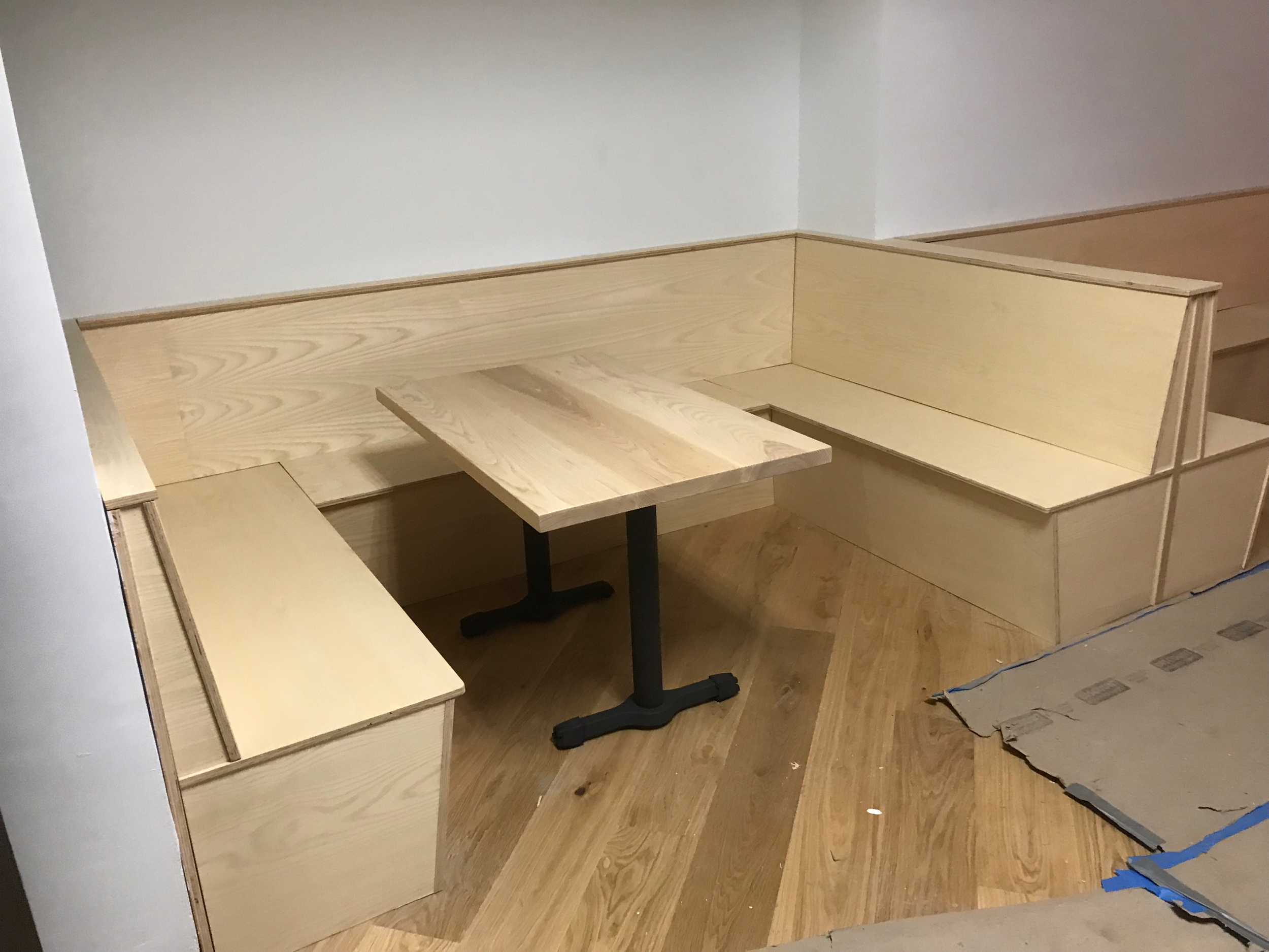 Custom wooden tables with metal legs designed for booths being installed with wooden booths.