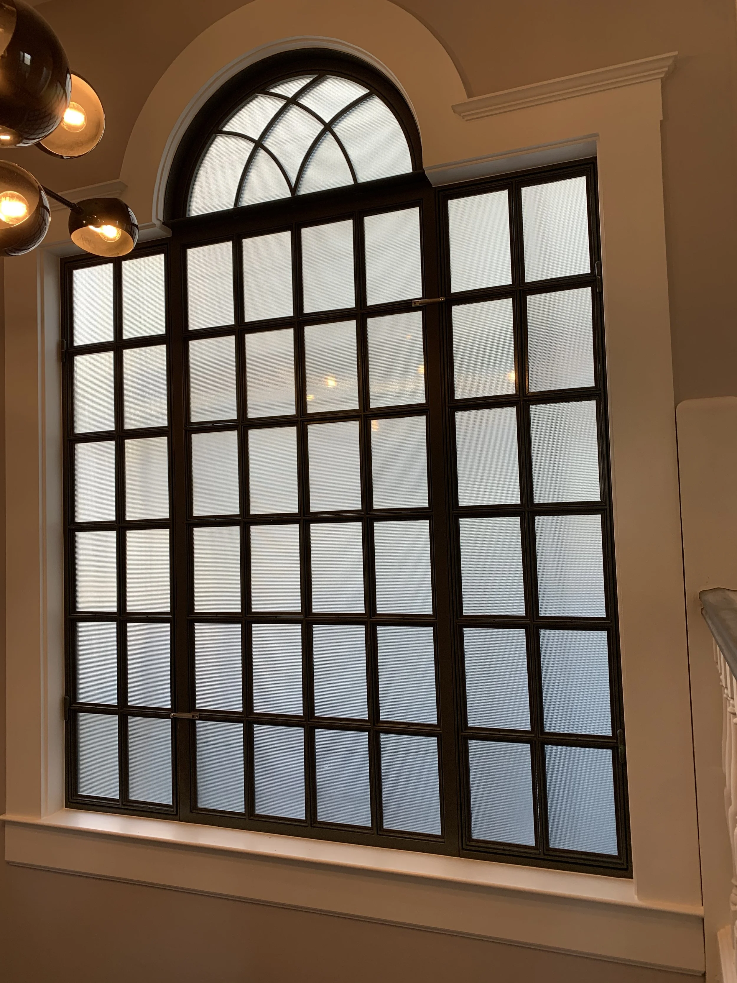A large square window broken into square glass by wooden strips. the top of the window has a semi-circle shape on top with cubed strips going through the semi-circle.