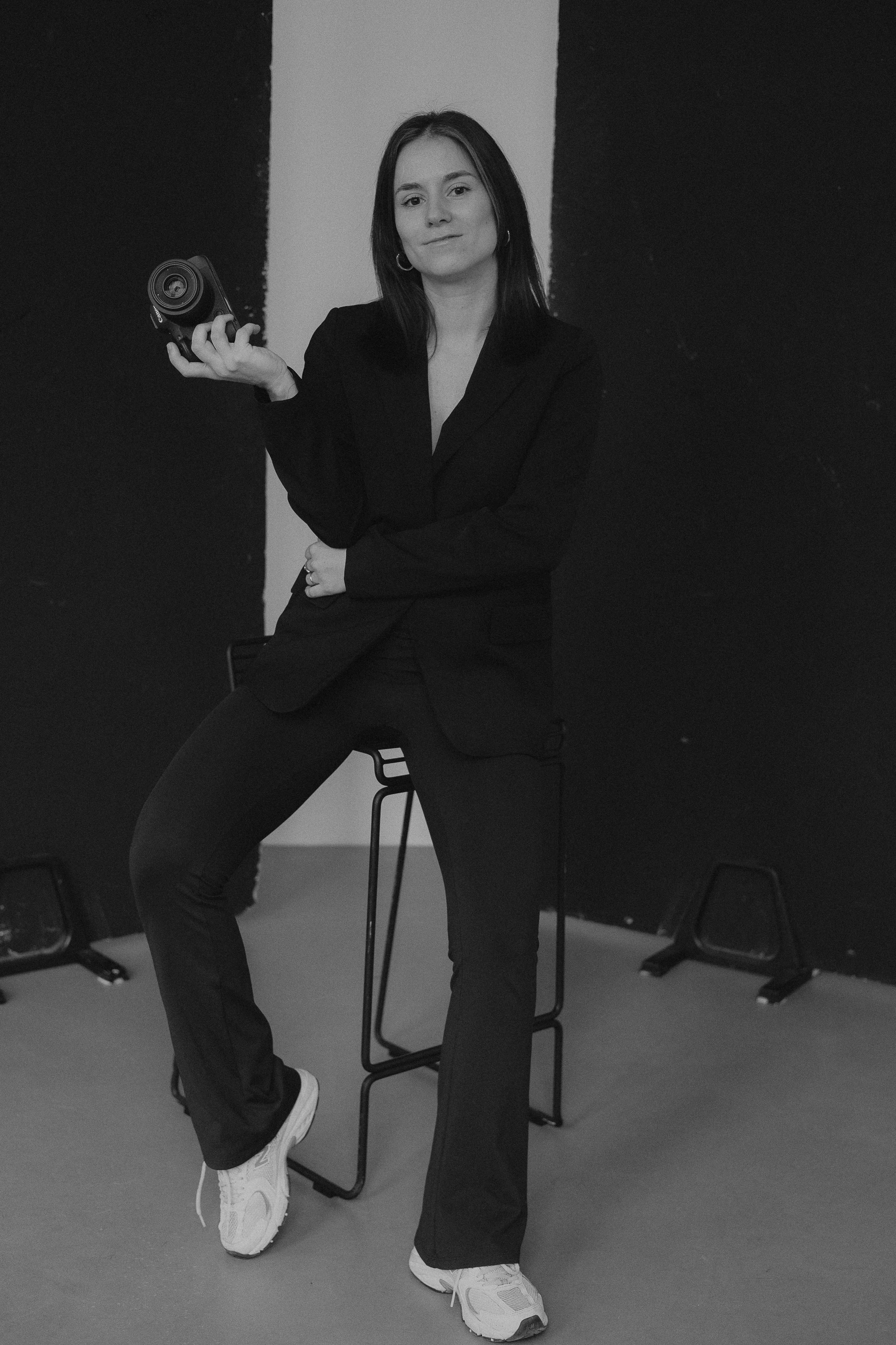 Schwarz-Weiß-Foto einer sitzenden Hochzeitsvideografin auf einem Hocker mit Kamera in der Hand.