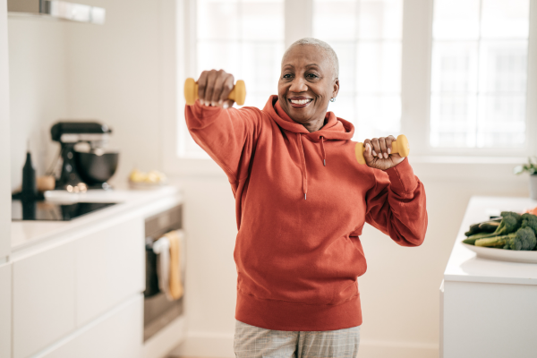 Woman using small yellow dumbbells in a bright kitchen.