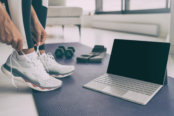A workout mat with small weights and a laptop top on, a female is putting on a pair of trainers