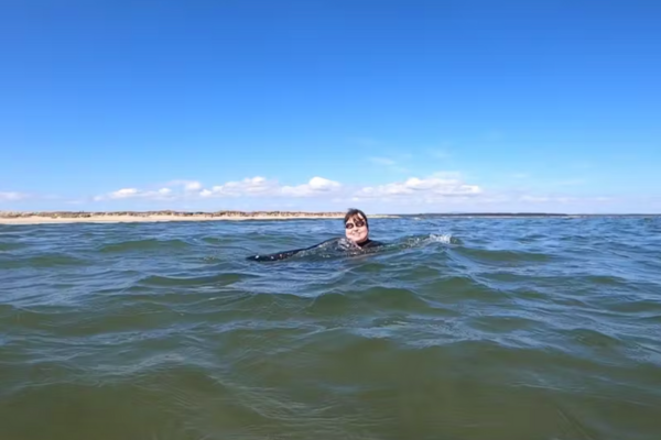 A woman is swimming in the sea wearing a wetsuit with blue skies above