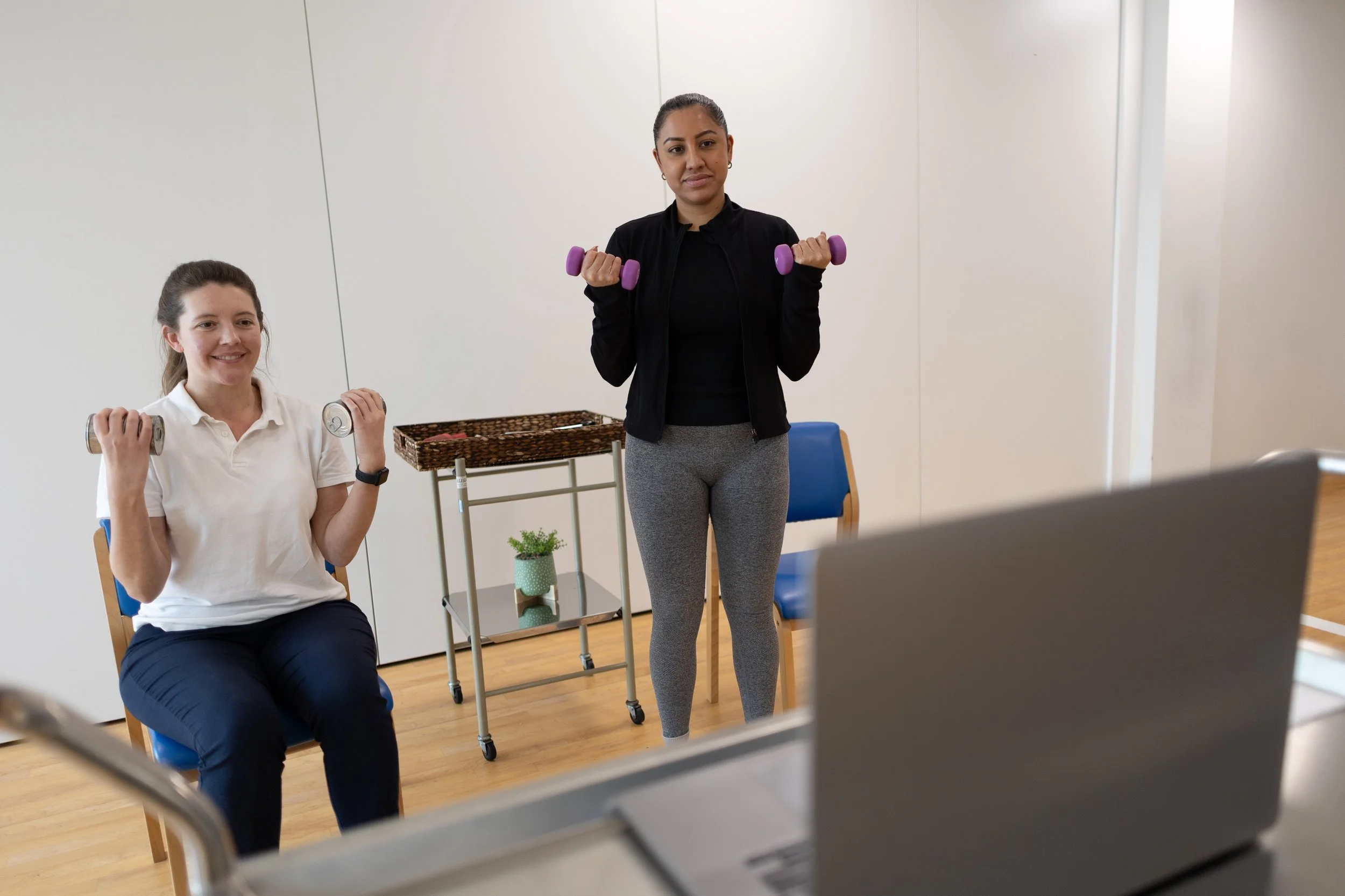 Two Kidney Beam instructors exercising with dumbbells during a virtual fitness class