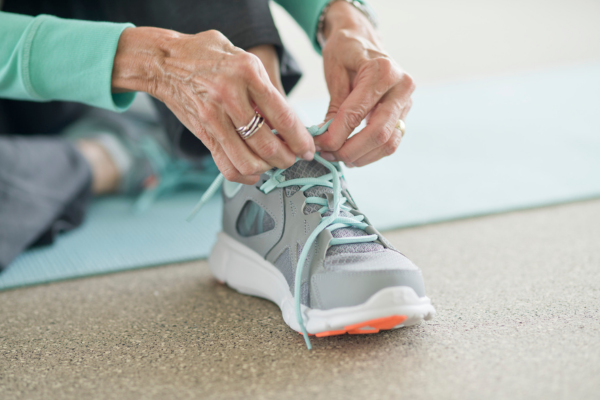 Image shows the hands of an older woman lacing up walking shoes