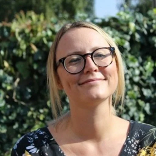 Jamie smiles against a leafy green background