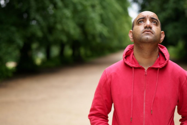 Kidney Beam and transplant recipient Fez is walking along a nature path in a red hoodie looking up