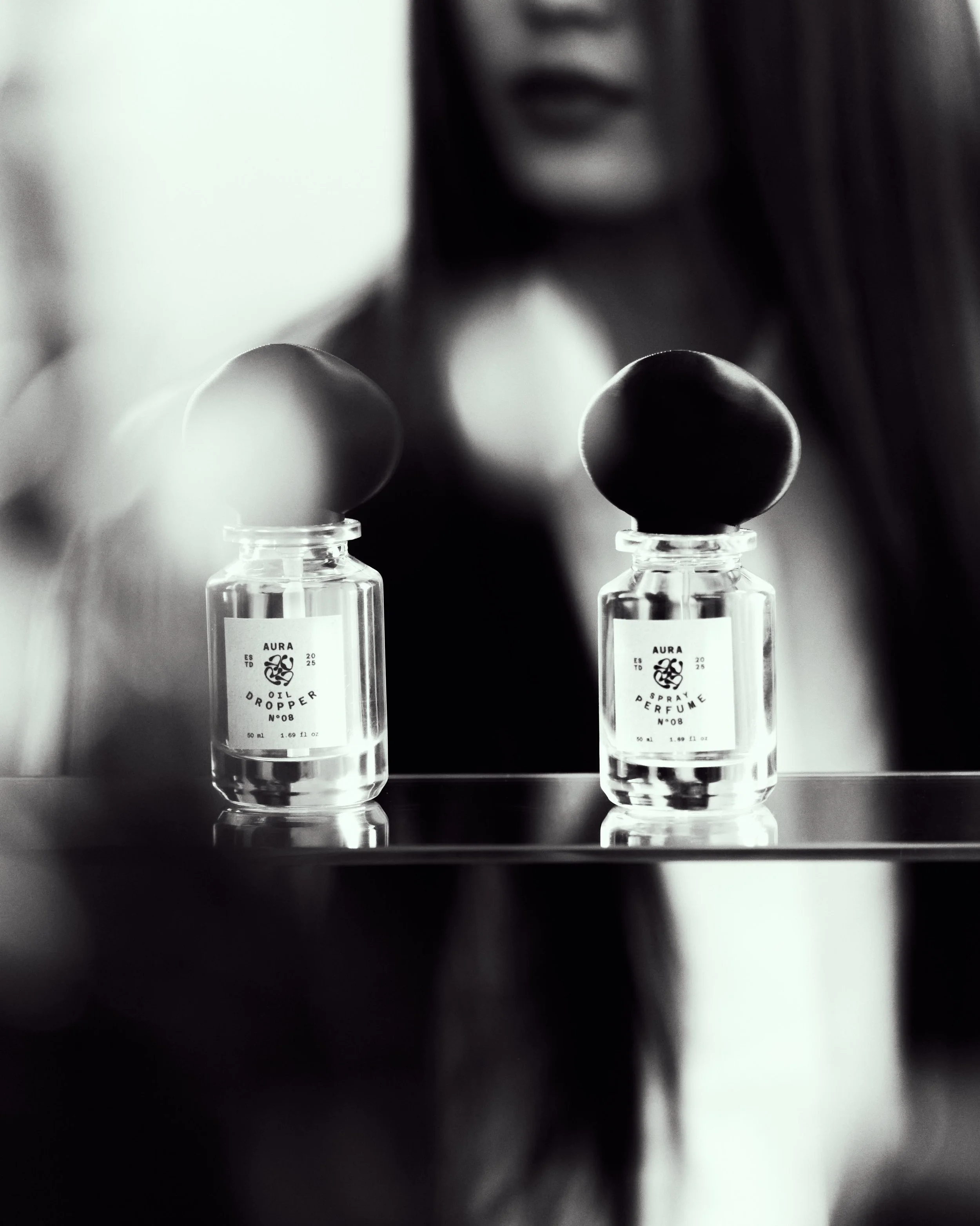 Due bottiglie di profumo con sfondo di una donna sfocata, in bianco e nero.