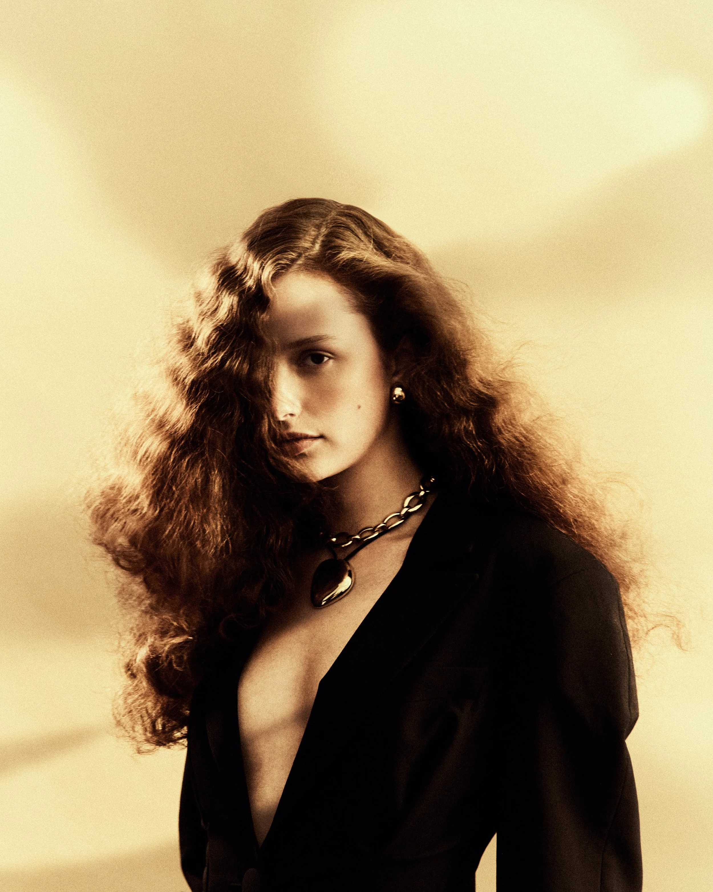 Ragazza con capelli ricci, indossa una giacca nera, una collana con pendente a forma di cuore e orecchini discop.