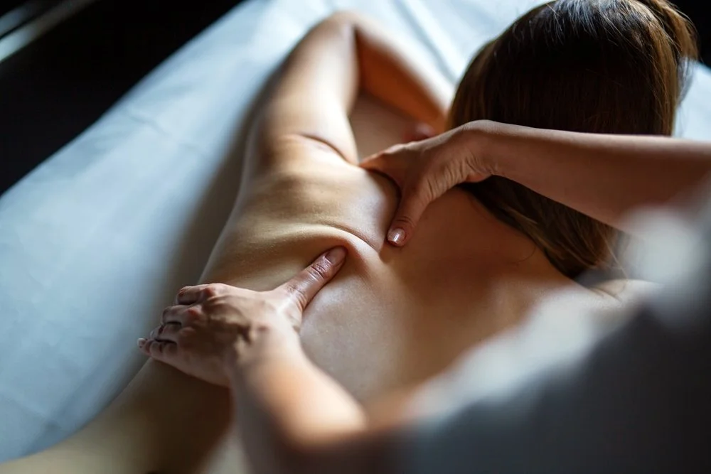 Une personne reçoit un massage thérapeutique dans un lit de massage, allongée sur le ventre, avec un masseur utilisant ses mains pour masser le dos.