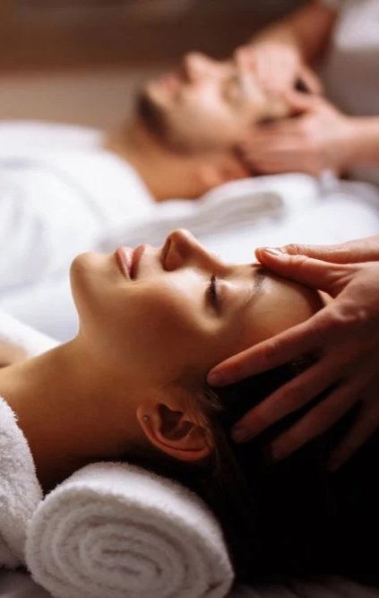 Une femme reçoit un massage facial, une autre personne se trouve en arrière-plan, également en train de recevoir un soin.