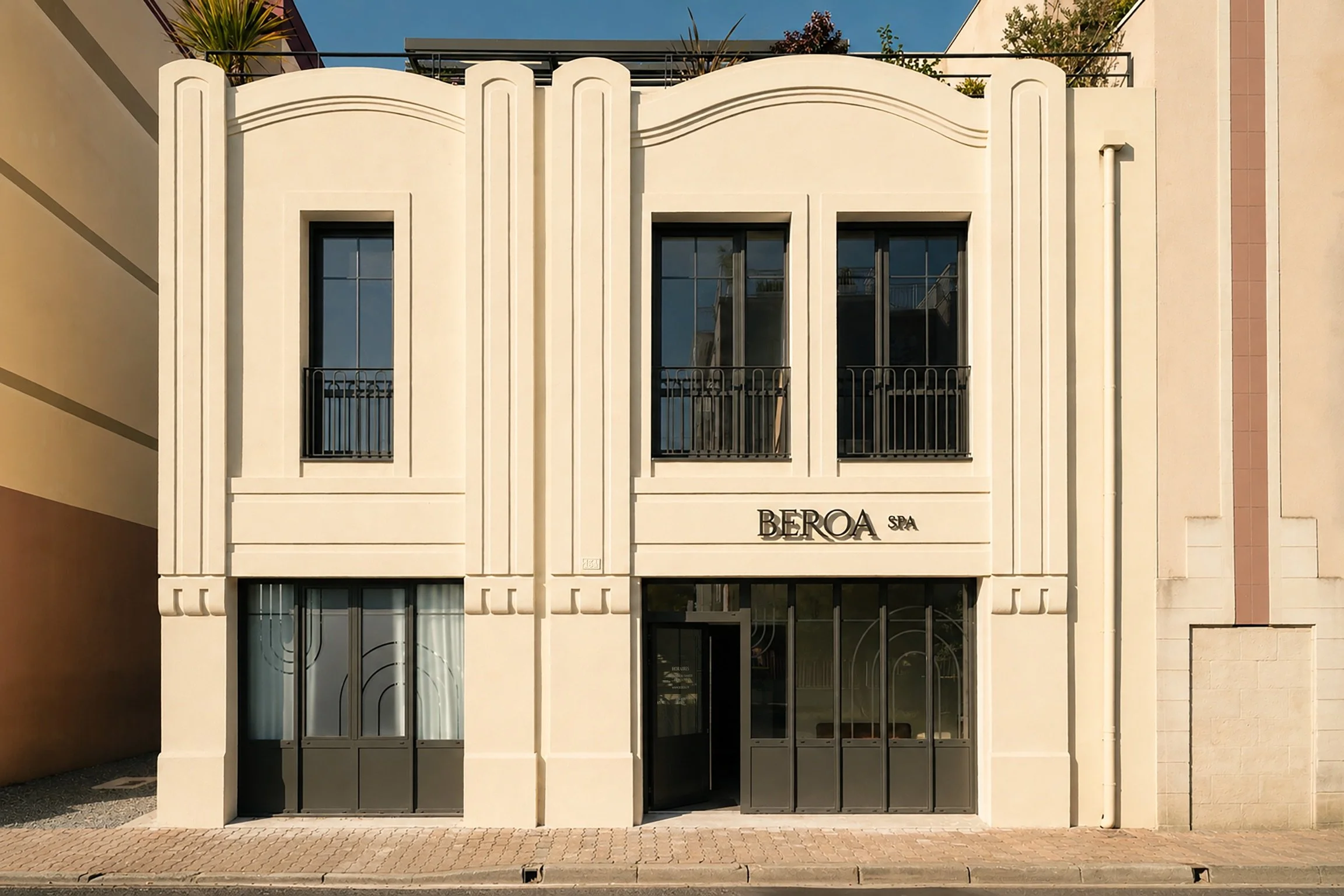 Façade d'un bâtiment moderne avec des fenêtres à vitres teintées, ornements en relief, balcon et un panneau indiquant 'BEROA SPA'.