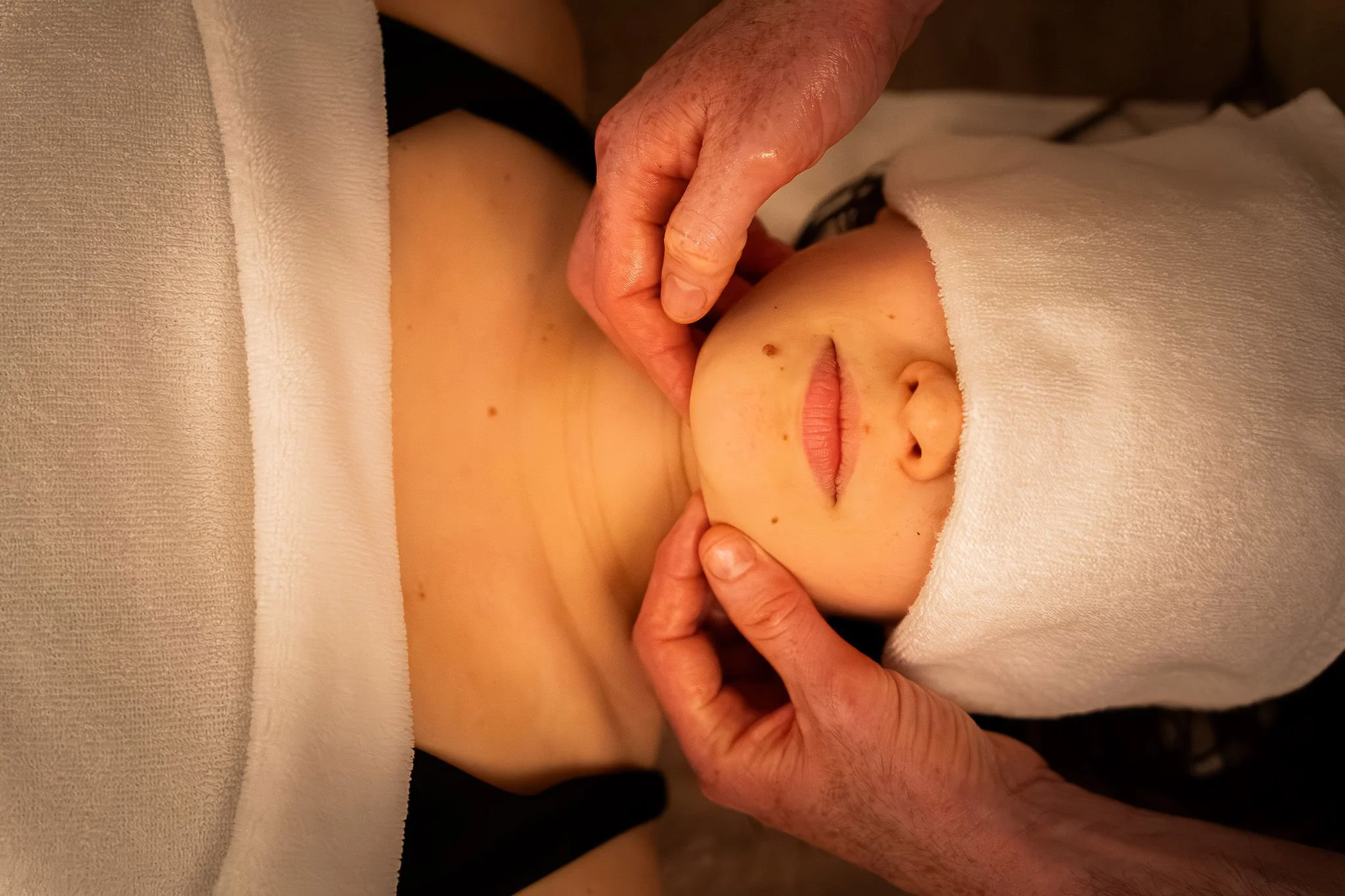 Une personne reçoit un massage, avec un massage étant effectué sur son ventre ou sa région abdominale, partiellement couverte par une serviette blanche au Spa Beroa.