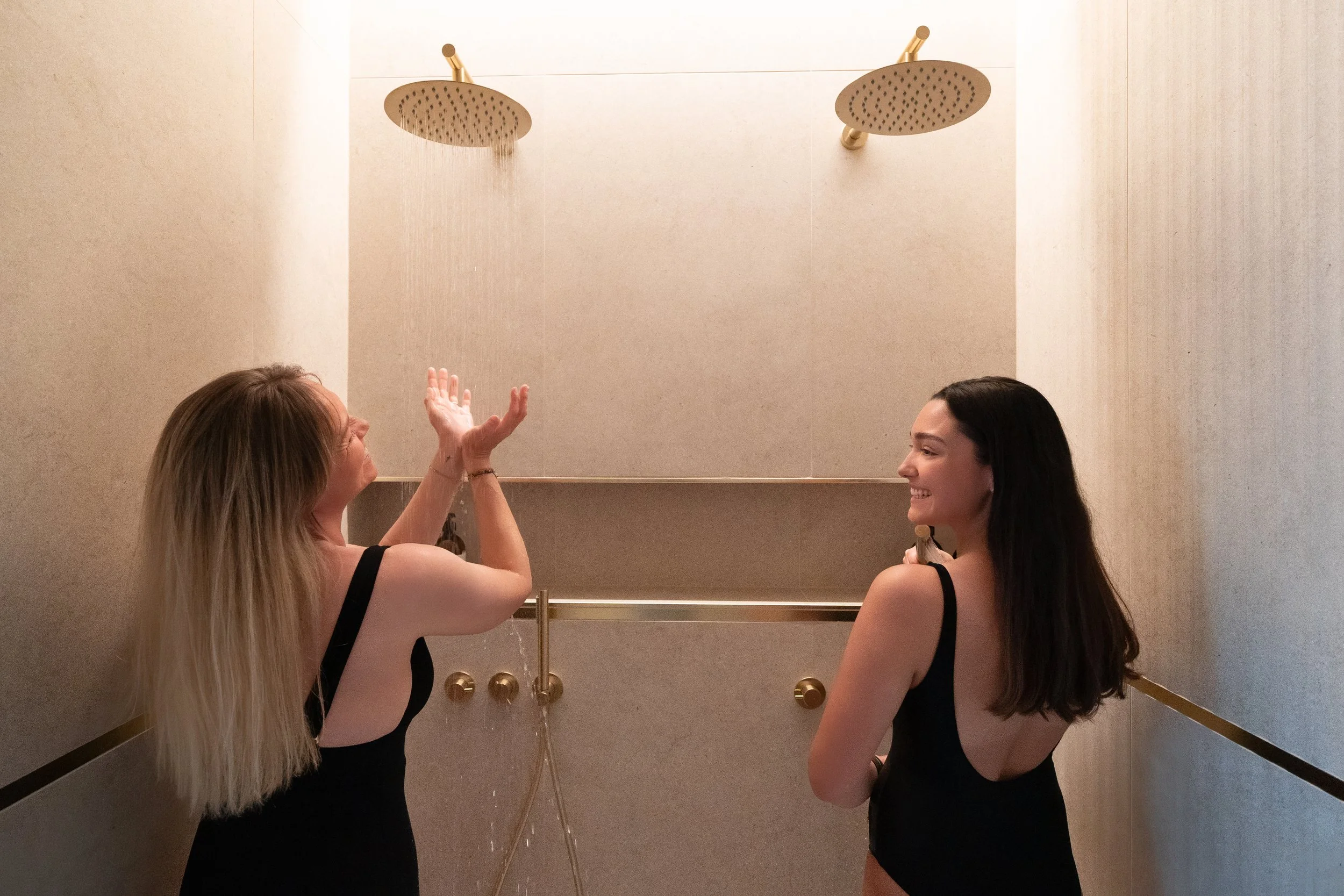 Deux femmes discutant sous une douche à l'intérieur d'une salle de bain spacieuse et élégante. Douches du Spa Beroa à Arcachon