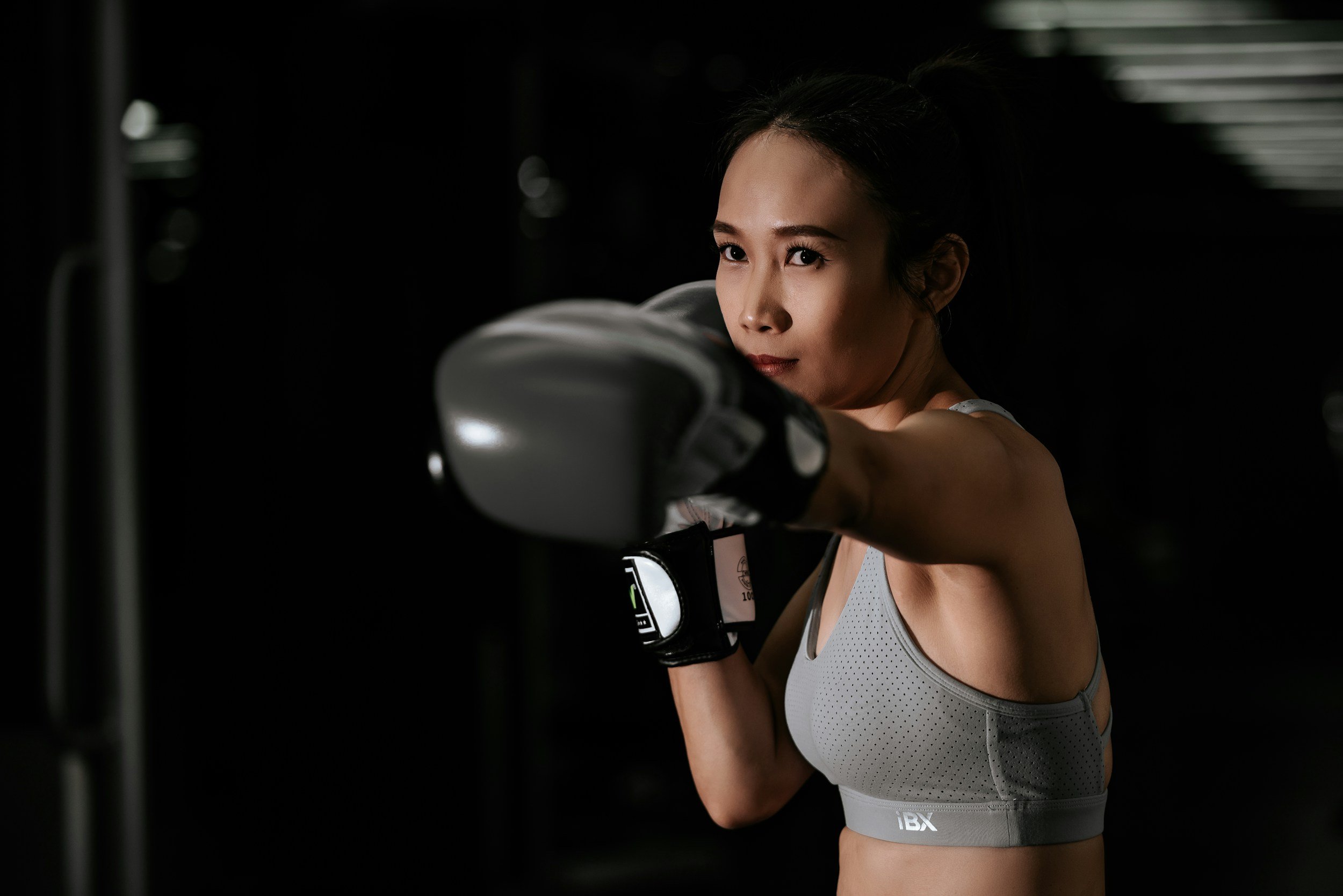 A woman in workout gear throws a punch in a boxing gym with a dark background.