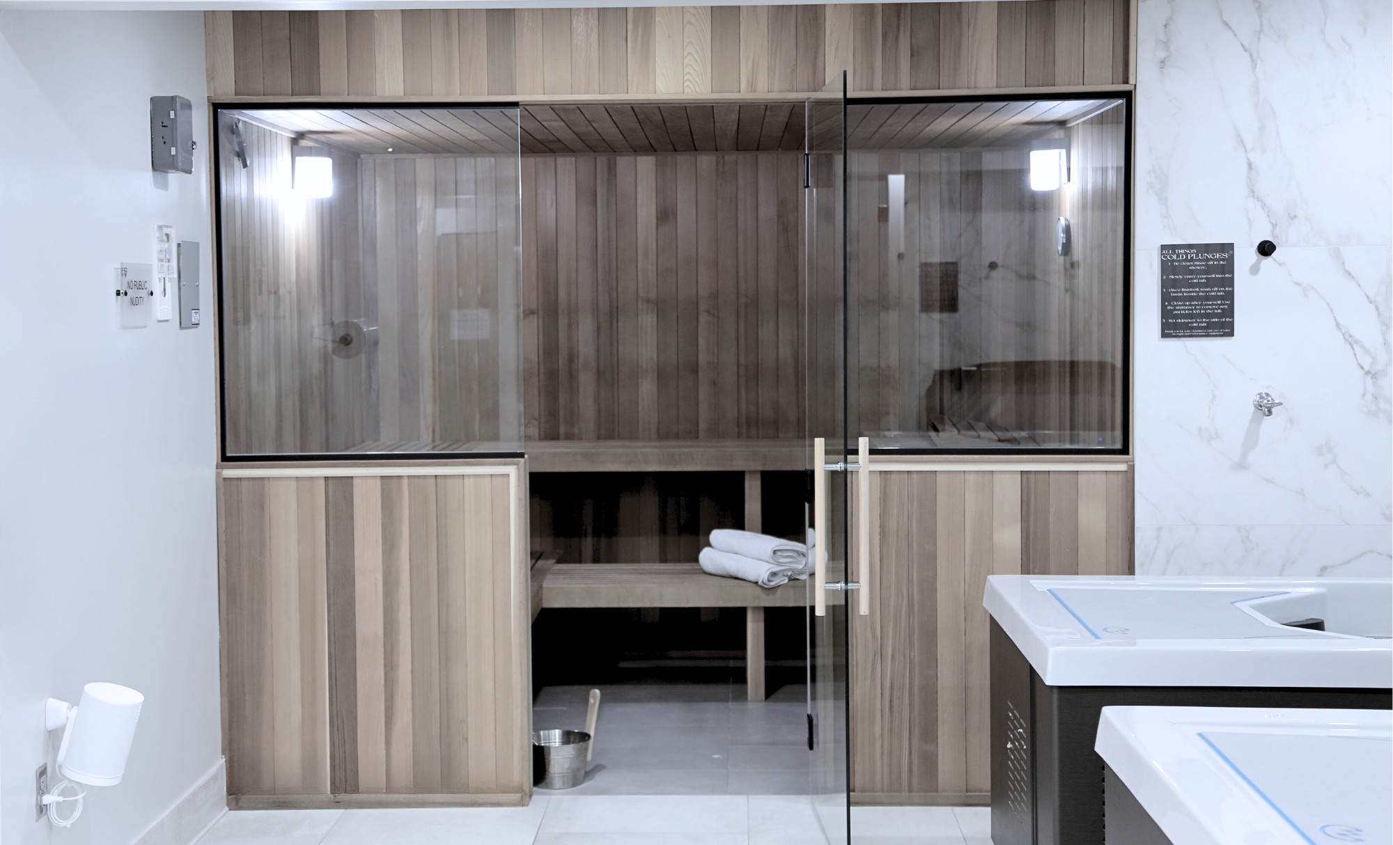 Commercial sauna room with wooden interior, glass door, towels, and a small bucket at the bottom.