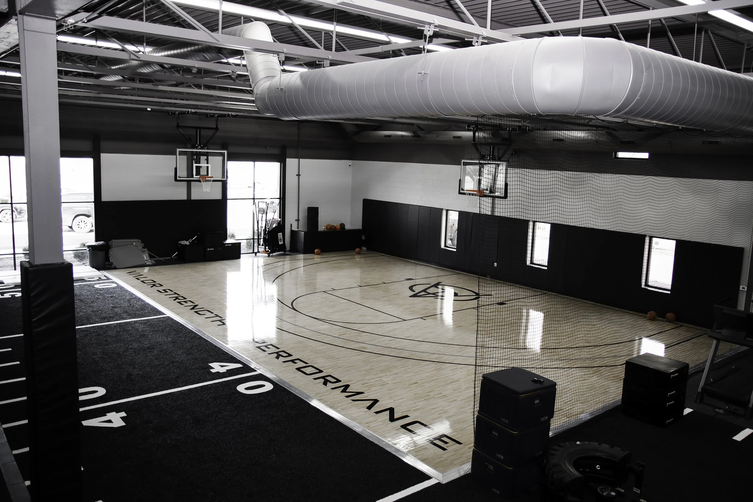 Indoor basketball court with black and white walls, basketball hoops, and a net, within a sports training facility.