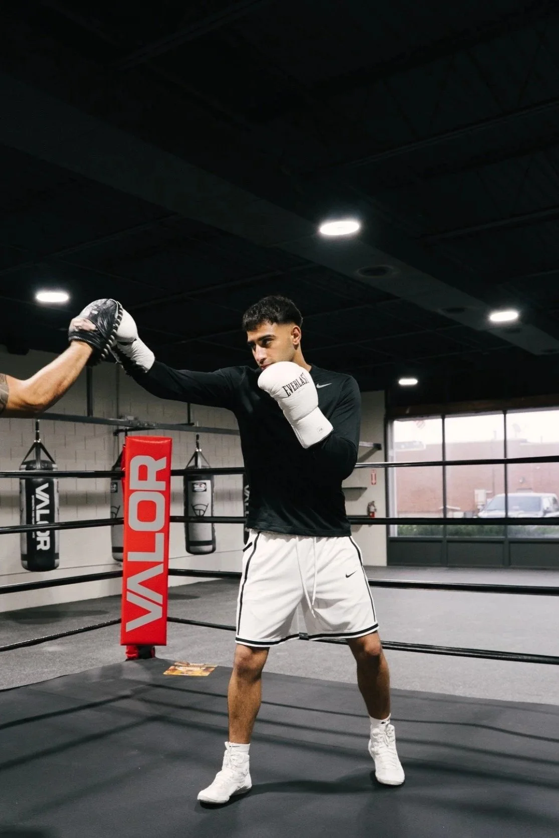 Young male boxer practicing with a trainer in a boxing gym, wearing boxing gloves and athletic clothes, inside a boxing ring.