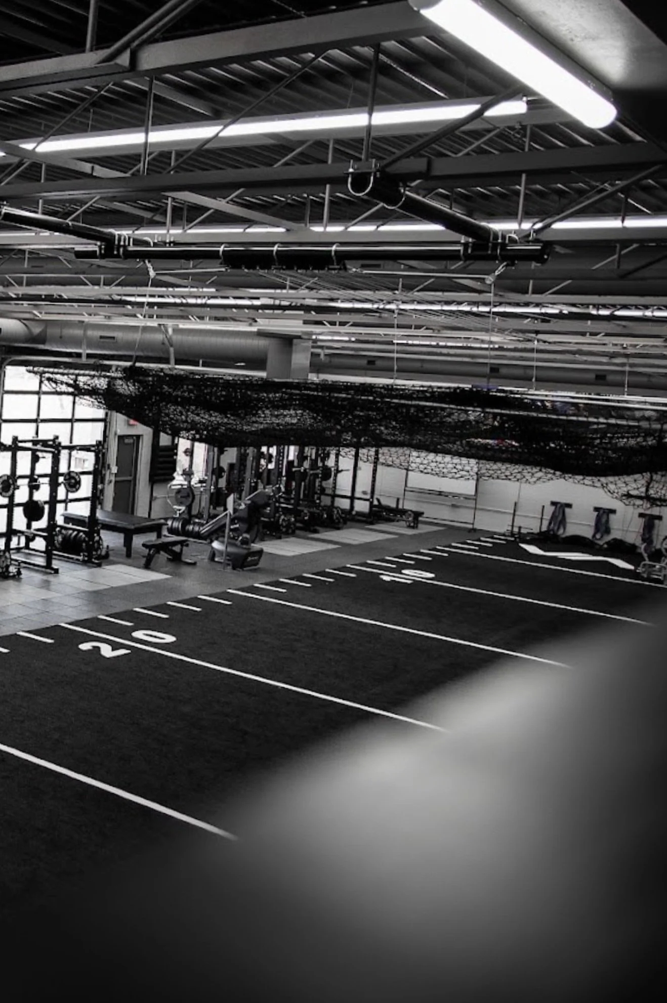 Empty indoor gym with black and white striped flooring, workout equipment, and a large overhead net or impact pad.