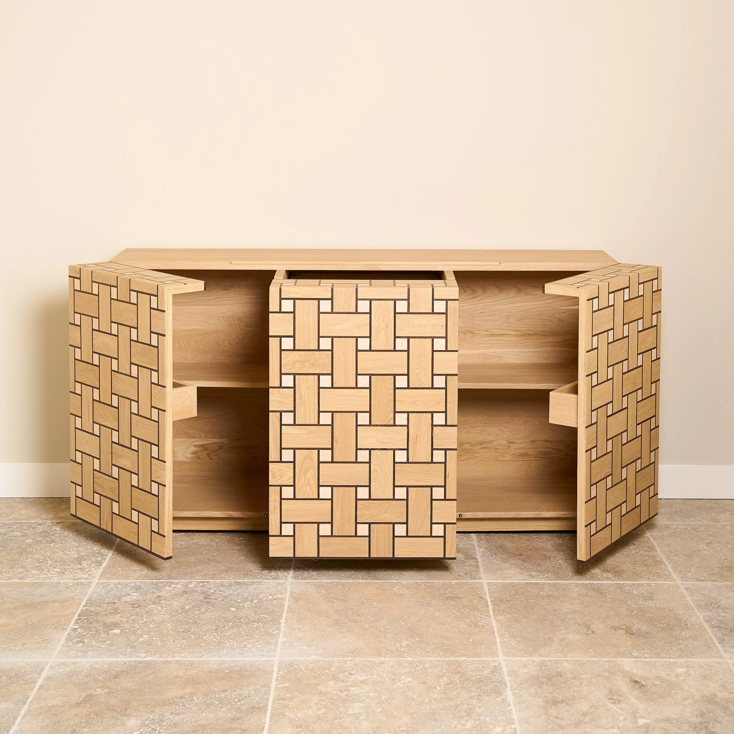 A wooden cabinet with a woven pattern design on the doors, open shelves inside, placed against a plain wall on a tiled floor.