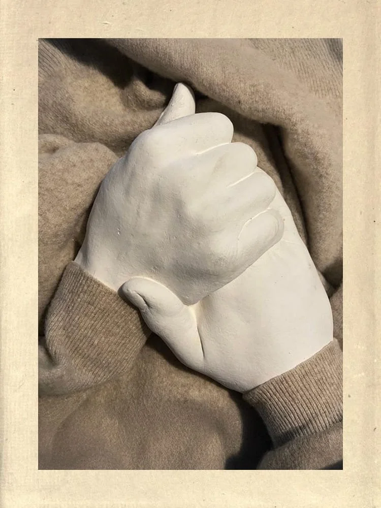 White sculptural hands gently holding each other, resting on soft fabric, symbolising connection and embodiment
